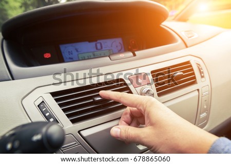 Driver hand tuning air ventilation grille, emergency flasher switch and light in modern car interior