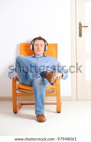 Man with closed eyes listening music with headphones sitting on chair at home
