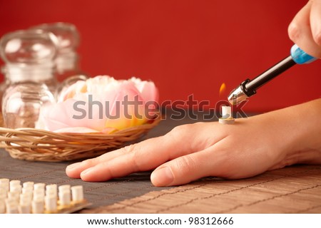 TCM Traditional Chinese Medicine. Hand lighting mini moxa stick, flower and natural herbs in glass jars in background.