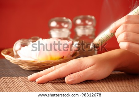 TCM Traditional Chinese Medicine. Hand applying moxa stick therapy, natural herbs in glass jars in background