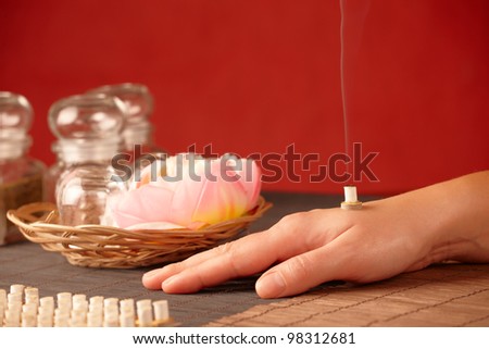 TCM Traditional Chinese Medicine. Smoking mini moxa stick on human hand, natural herbs in glass jars in background