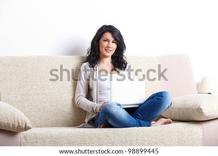 Portrait of a beautiful young woman sitting on sofa and using laptop in home