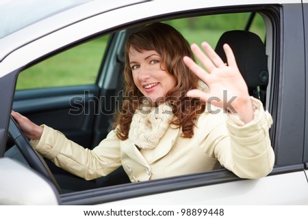 Pretty young woman sitting car looking out of window, waving and smiling