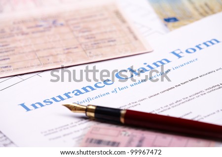 Blank insurance claim form and other papers like ID or vehicle documents and pen lying on desk