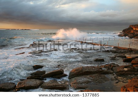 Surise at the beach, waves crashing, rocks glowing, clouds falling, water rolling, stunning shot.