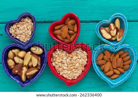 Ceramic heart shape bowls with healthy breakfast items: whole oatmeal, almonds and Brazil nuts