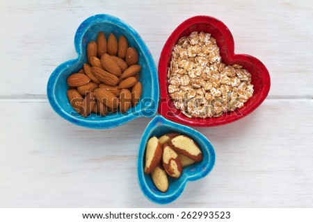 Ceramic heart shape bowls with healthy breakfast items: whole oatmeal, almonds and Brazil nuts