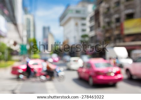 Blurred unfocused city view at day time. Unfocused cars in the way. Unfocused pink car.