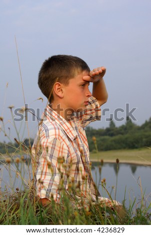 The boy sits on coast of the river and looks afar