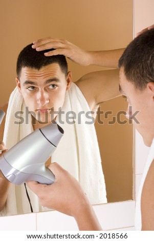 reflexion of young man in the bathroom\'s mirror using hair drier