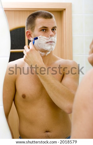 reflexion of shaving young man in the bathroom\'s mirror