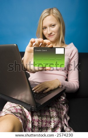 Young woman sitting on the black sofa with laptop and credit card in her hand. Focus on the card. Face unfocus.