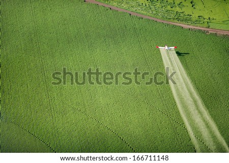 An aerial view of a crop duster as it flies low, spraying farm fields