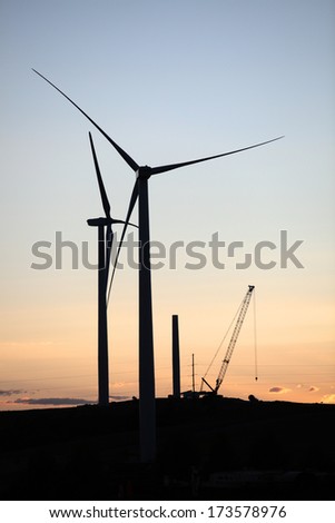 Silhouettes of large power generating windmills under construction, taken at sunset.