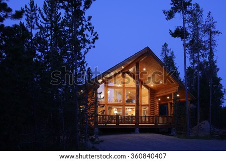 The exterior at dusk of a modern log cabin, in the mountains.