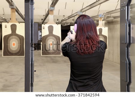 A woman firing a hand gun at an indoor gun range.