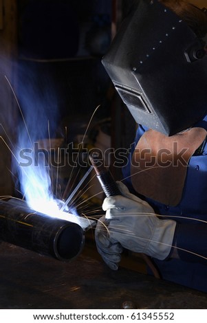 A man arc welding.  Sparks are flying through the air, and smoke is being drawn out the exhaust system.