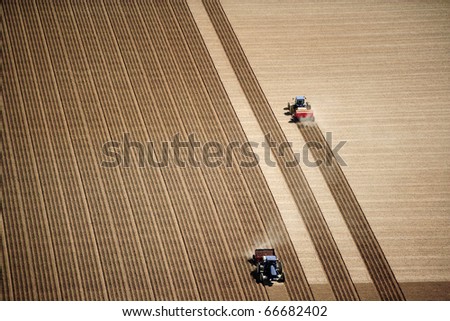 An aerial view of 2 tractors planting potatoes in the fertile farm fields of Idaho, during the spring.