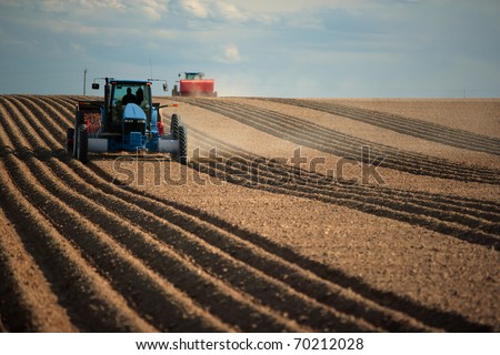 An image of two Tractors planting potatoes in the fertile farm fields of idaho.
