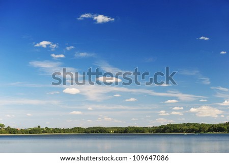 calm water of  lake, woods on other side and  blue sky. landscape
