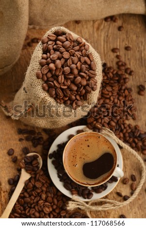 coffee beans in jute sack behind  cup of black coffee
