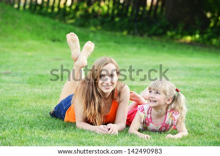 young mother with her daughter lie on grass . summer day.
