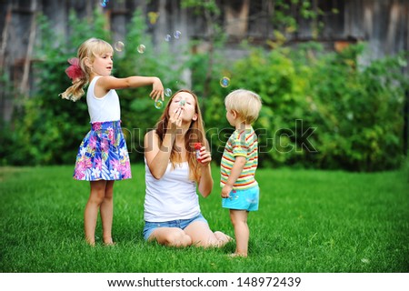 Mother And Her Children Play With Bubble Blower On Green Lawn