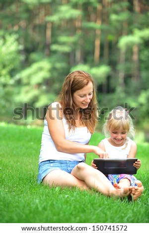 young mother with her daughter  looking at screen of laptop. summer day.