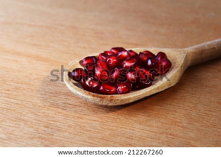 Ripe pomegranate seeds in wooden spoon