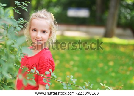 little girl near flower\'s bush in park.
