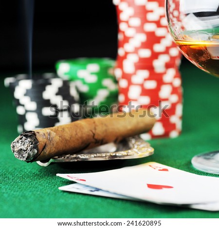 Cigar, chips, drink and playing cards on green