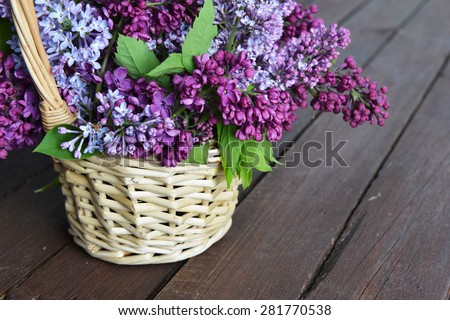 basket with  branch of lilac on wooden background