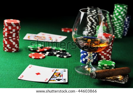 Cigar, chips for gambling, drink and playing cards on green