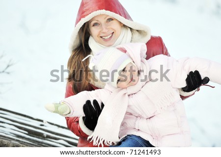 young mother with her daughter sitting on wooden bench in  park. winter day