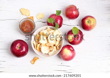Red apple with leaf and slice dried apples on a white wood background.
