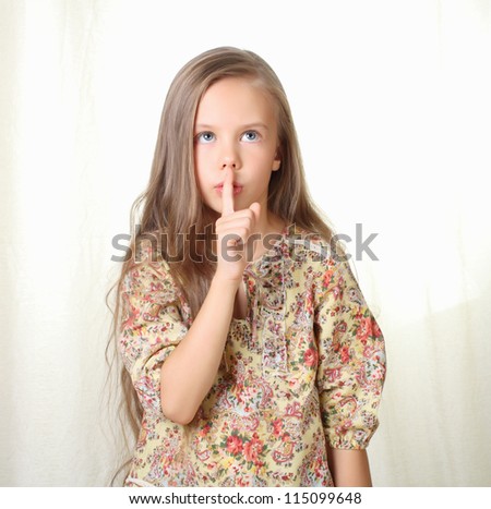 Little blond girl keeping silence holding forefinger near lips