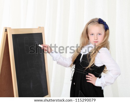 Little girl writing on black board by chalk and looking to camera