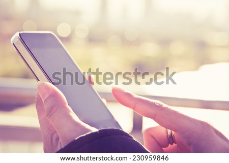 Women hand holding a smart phone with sunrise background