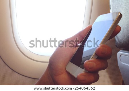 business man sits in airplane watching his cell phone