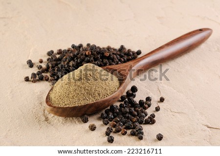 milled black pepper,heap of powdered black pepper on a wooden spoon and pepper corns