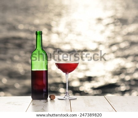 Bottle and glass of red wine on the table against the sea or ocean