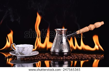 Fired cup of coffee with coffee beans and turk on dark background