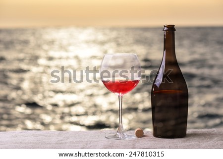 Bottle and glass of red wine on the linen table against the sea or ocean