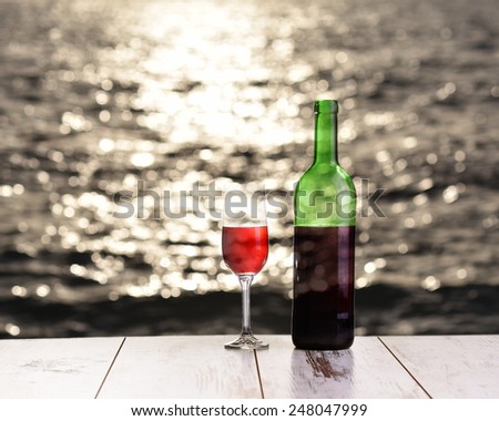 Bottle and glass of red wine on the linen table against the sea or ocean on the sunset