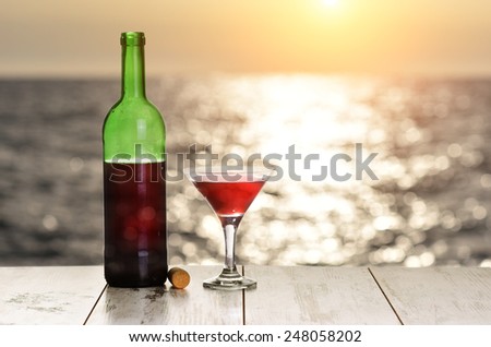 Bottle and glass of red wine on the linen table against the sea or ocean on sunset