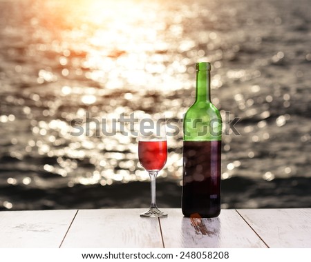 Bottle and glass of red wine on the linen table against the sea or ocean on sunset