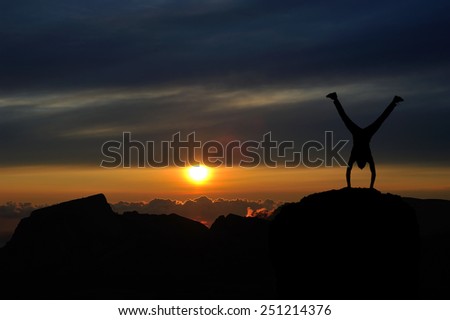 Silhouette of man at the top of the mountain on sunset. Man stands on his hands at the top of the mountain. Beautiful landscape.