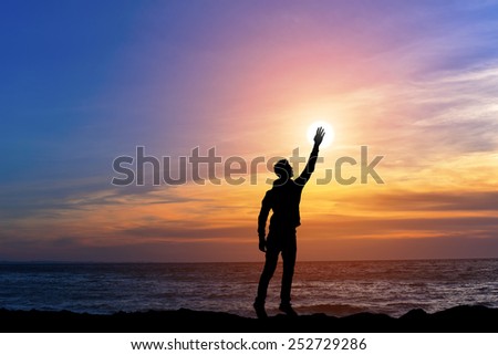 silhouette man holding sun on the sea ocean bank, happy man on beach with hand up on sunset background