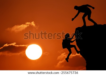 The joint work teamwork of two people man and girl travelers help each other on top of a mountain climbing team, a beautiful sunset landscape with big sun