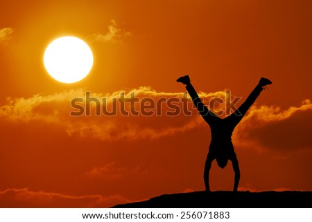 Silhouette of man at the top of the mountain on sunset. Man stands on his hands at the top of the mountain. Beautiful landscape.